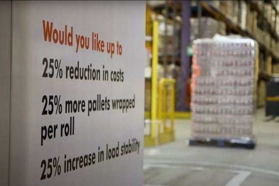 A sign saying if you would like 25% reduce cost, more pallet wrap per roll and increase in load stability with inside of warehouse in background